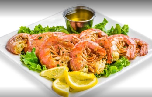 A plate of large shrimp on a bed of lettuce, garnished with lemon slices and a small cup of dipping sauce.