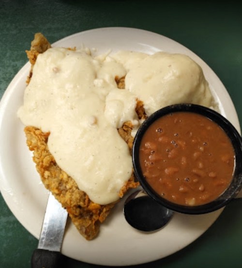 A plate featuring fried chicken smothered in creamy gravy, served with a side of baked beans.