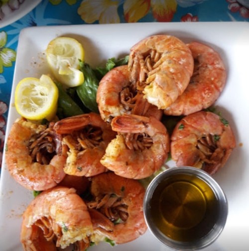 A plate of large shrimp with lemon slices and a small bowl of dipping sauce, garnished with greens.
