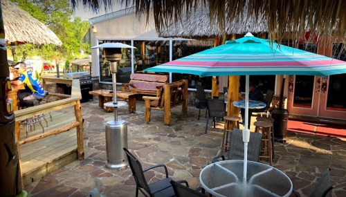 Outdoor patio area with wooden furniture, colorful umbrellas, and a thatched roof, creating a relaxed dining atmosphere.