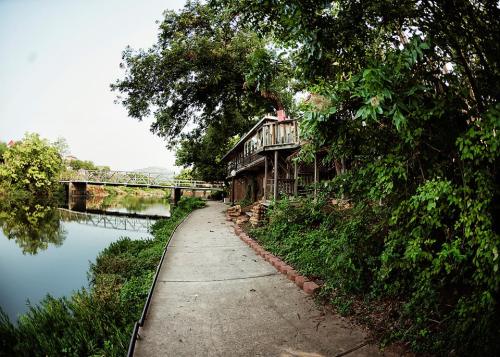 A scenic riverside path lined with greenery, leading to a wooden structure overlooking the water.
