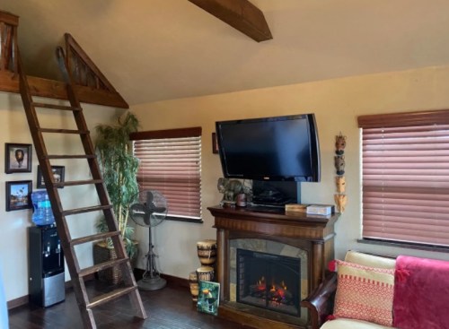 Cozy living room with a wooden ladder, TV, fireplace, and decorative items, featuring warm lighting and wooden accents.