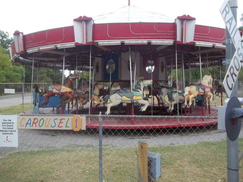 A colorful carousel with painted horses, surrounded by a fence and a sign labeled "Carousel 1."