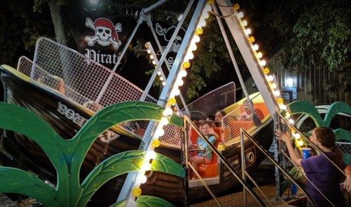 A pirate-themed amusement ride with colorful lights and palm tree decorations, featuring excited riders.