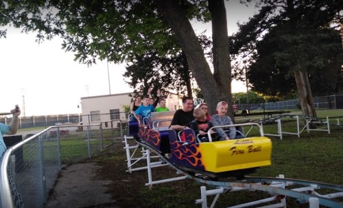 A group of people enjoying a ride on a small roller coaster called "Fire Ball" at an amusement park.