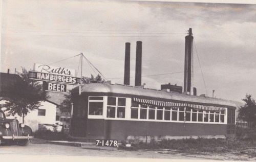Historic diner with a sign reading "Ruth's Hamburgers Beer," featuring a vintage streetcar design and industrial background.