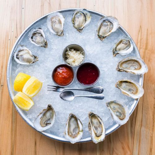 A platter of fresh oysters on ice, garnished with lemon wedges and served with cocktail sauce and mignonette.