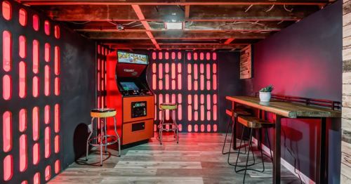 A retro arcade corner featuring a Pac-Man machine, bar stools, and red-lit walls.
