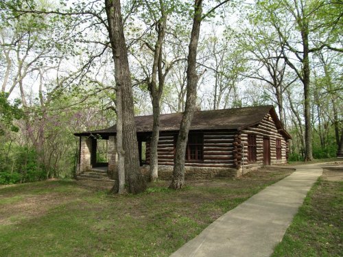 A rustic log cabin surrounded by trees, with a pathway leading to the entrance.
