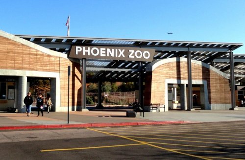 Entrance to the Phoenix Zoo, featuring a large sign and visitors waiting outside on a sunny day.