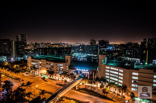 A nighttime cityscape featuring the Diplomat Hotel, with lights reflecting on water and buildings in the background.
