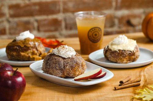 Three delicious pastries topped with whipped cream, served on white plates with apple slices and a drink in the background.