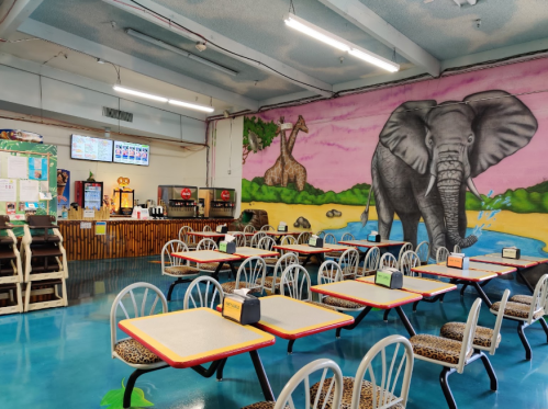 Colorful restaurant interior featuring tables, chairs, and a large elephant mural on the wall.