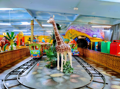 A colorful indoor amusement area featuring a giraffe statue, train tracks, and vibrant decorations.