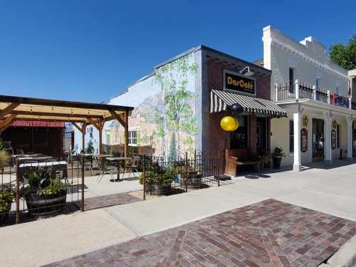 A quaint café with outdoor seating, surrounded by colorful murals and a clear blue sky.