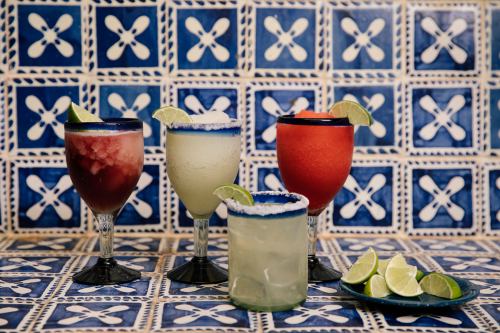 Four colorful cocktails with lime wedges, set against a blue and white tiled background.
