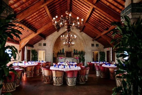 Elegant dining room with a high wooden ceiling, chandelier, and tables set with blue napkins and floral centerpieces.