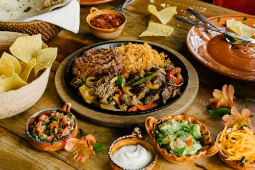 A vibrant plate of fajitas with beef, peppers, rice, refried beans, and sides of salsa, guacamole, and tortilla chips.