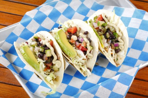 Three tacos filled with black beans, lettuce, tomatoes, and lime, served on a blue and white checkered paper.