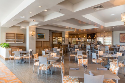 Modern restaurant interior with orange and gray decor, featuring tables, chairs, and a bar area in the background.
