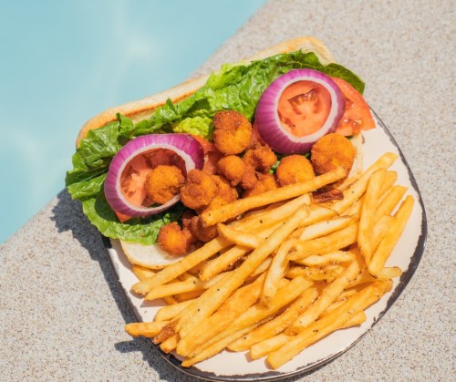 A plate with a sandwich topped with lettuce, tomato, onion, and fried items, served with a side of golden fries.