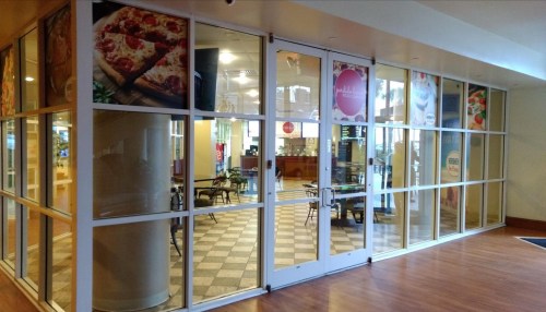 A glass storefront with a view of a cafe interior, featuring tables and promotional posters on the windows.
