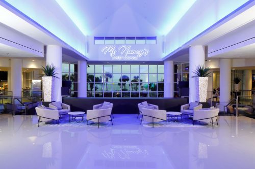 Modern lobby lounge with blue lighting, stylish seating, and large windows showcasing a view outside.