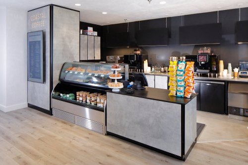 A modern coffee shop counter with pastries, coffee machines, and a menu board in a bright, minimalist setting.