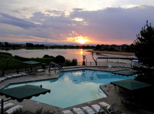 A serene sunset over a lake, with a swimming pool and lounge chairs in the foreground.