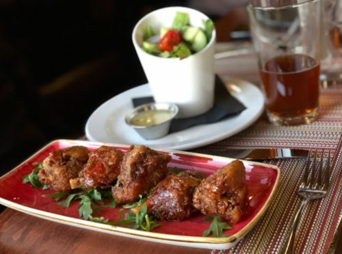 A plate of crispy fried chicken wings on a bed of greens, with a side salad and a drink in the background.