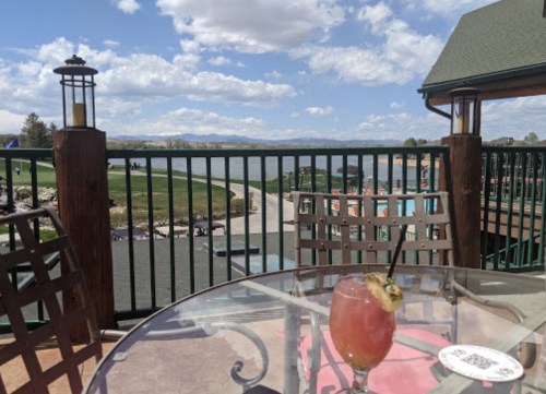 A refreshing cocktail sits on a table with a scenic view of a lake and cloudy sky in the background.
