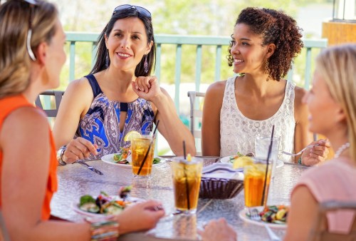 A group of four women enjoying a meal together at a restaurant, smiling and engaged in conversation.