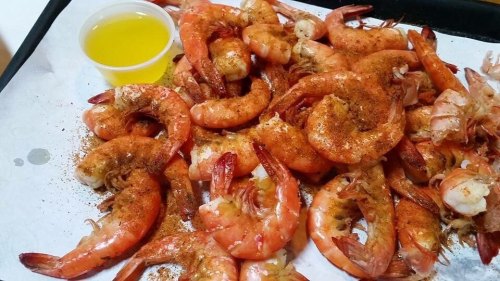 A pile of seasoned shrimp on a tray, accompanied by a small cup of yellow dipping sauce.