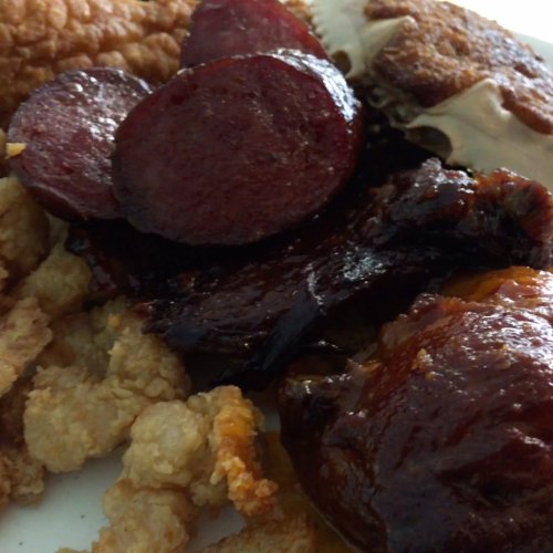 A close-up of a plate featuring various meats, including sausage slices, ribs, and fried seafood.