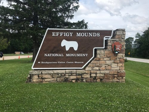 Sign for Effigy Mounds National Monument, featuring a stylized animal shape and information about the visitor center.