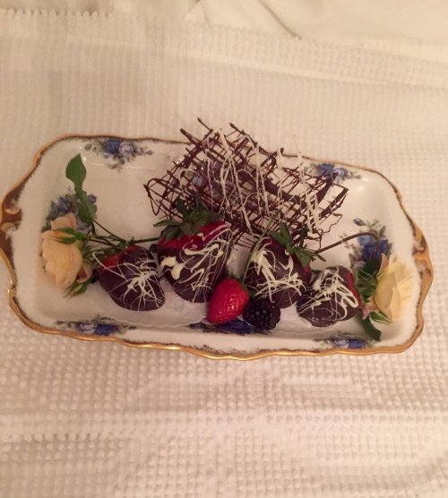 A decorative plate with chocolate-covered strawberries, blackberries, and delicate chocolate curls, garnished with flowers.