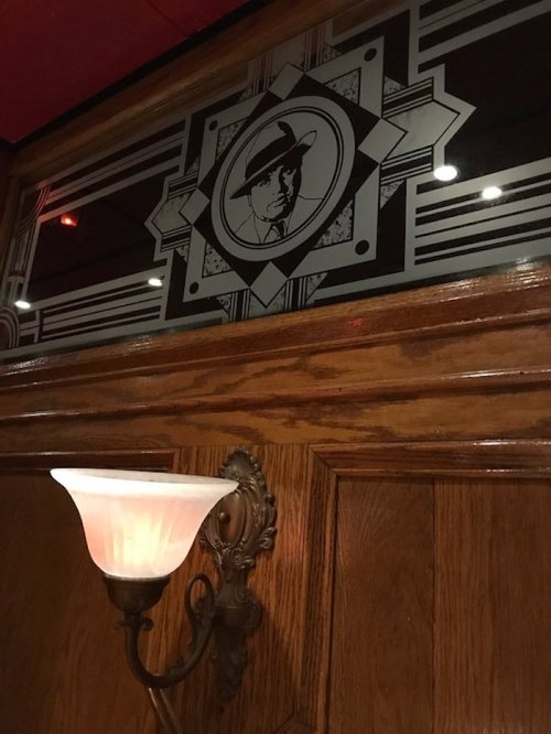 A vintage-style wall lamp beside a decorative glass panel featuring a man's portrait in a hat.