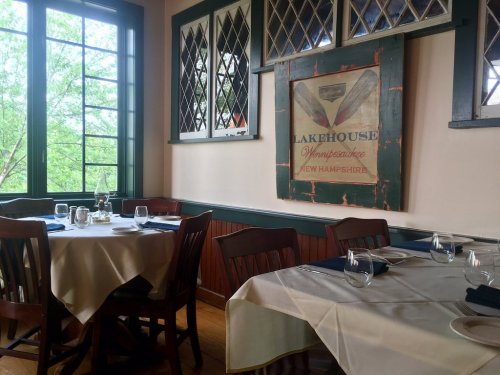 Cozy restaurant interior with wooden tables, white tablecloths, and a vintage Lakehouse sign on the wall.