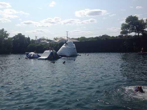 People swimming near inflatable water structures in a lake on a sunny day.