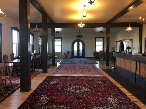 A spacious lobby with wooden beams, patterned rugs, and seating areas, featuring large windows and a reception desk.