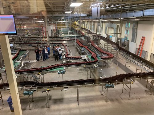 A large industrial facility with conveyor belts and workers gathered in the center, surrounded by machinery and equipment.