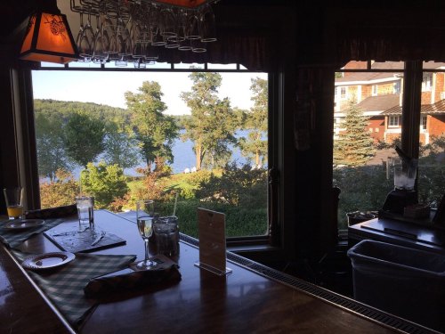 A view from a bar window overlooking a lake and trees, with glasses and a blender on the counter.