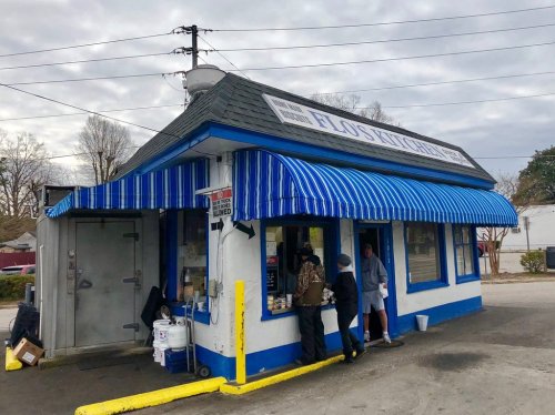 A small, blue and white food stand with a striped awning, featuring customers ordering at a window.