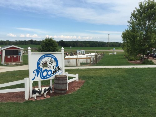 Sign for "MOOville" creamery with a cow statue, grassy area, and farm buildings in the background under a blue sky.