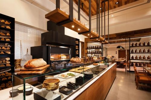 A modern restaurant interior featuring a display of bread, an oven, and shelves with jars and wooden accents.