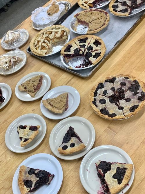 A variety of pies and pie slices on plates, including fruit-filled and crumb-topped options, displayed on a wooden table.