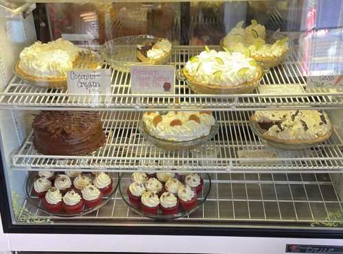 A display case filled with various desserts, including pies, cakes, and cupcakes, all topped with cream and decorations.