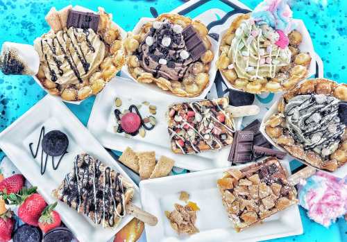 A colorful assortment of waffle bowls filled with various ice cream flavors, toppings, and cotton candy on a vibrant background.