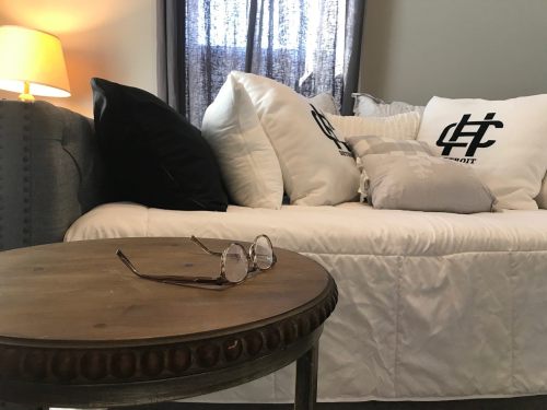 A cozy living room scene featuring a sofa with decorative pillows and a wooden side table with glasses resting on it.