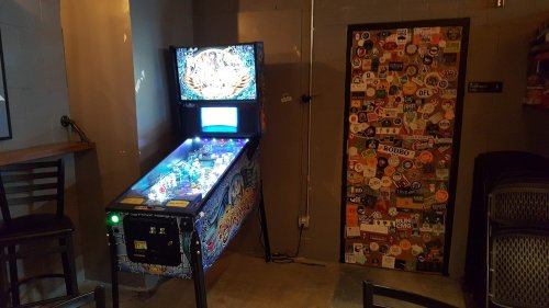A colorful pinball machine next to a door covered in various stickers in a cozy indoor space.